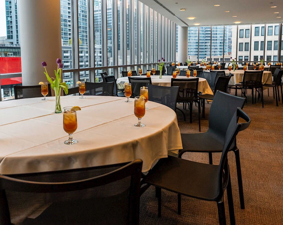 Glasses of iced tea and fresh cut flowers adorn round dining tables in the Small North Lounge at the University of Chicago Gleacher Center