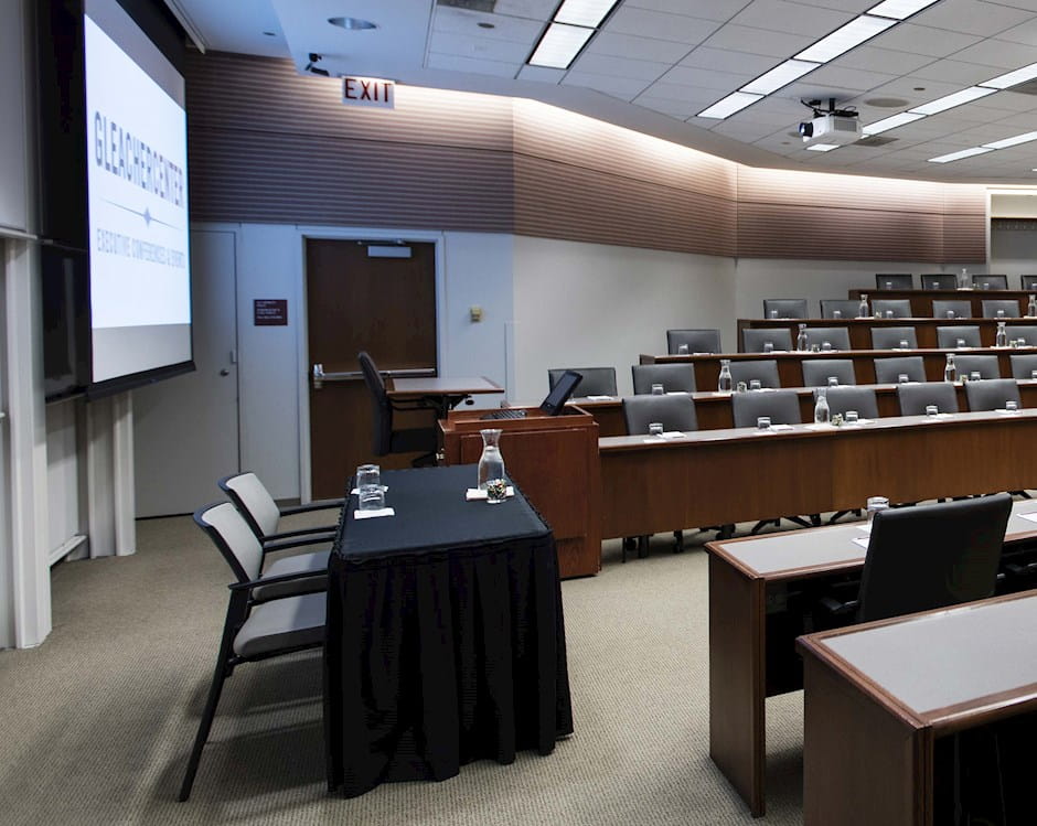 Tiered lecture room at the University of Chicago Gleacher Center with tables and chairs form a U-shape facing a presenters' table