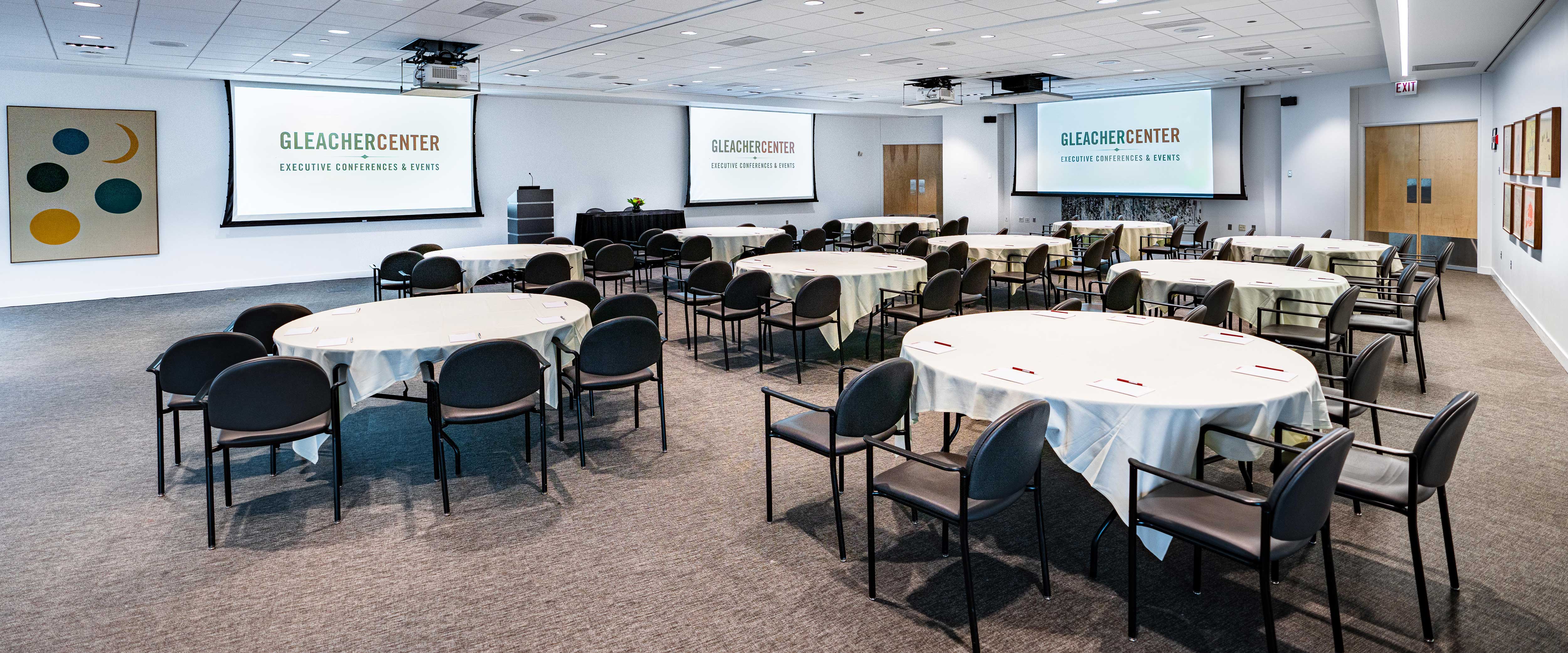 Gleacher Center conference area staged for event with projectors, tables, and chairs with notepads