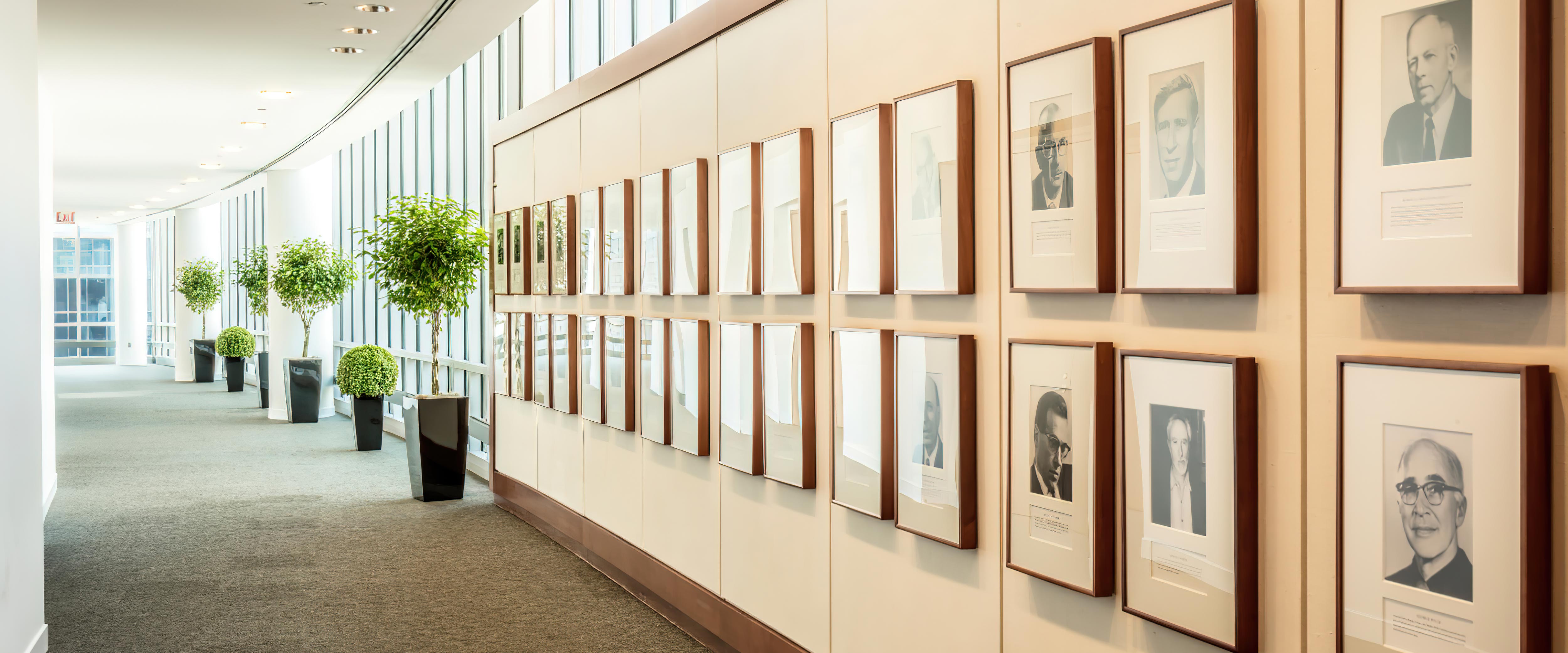 Looking down the Gleacher Center's Nobel Wall toward a bight hallway with plants and trees