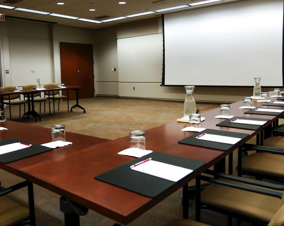 Angled view of warm wood tables in a U-shape facing a projector screen
