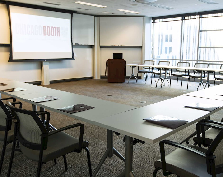 Room 422 in Gleacher Center showing the full semi-circle of desks and chairs with a projector screen