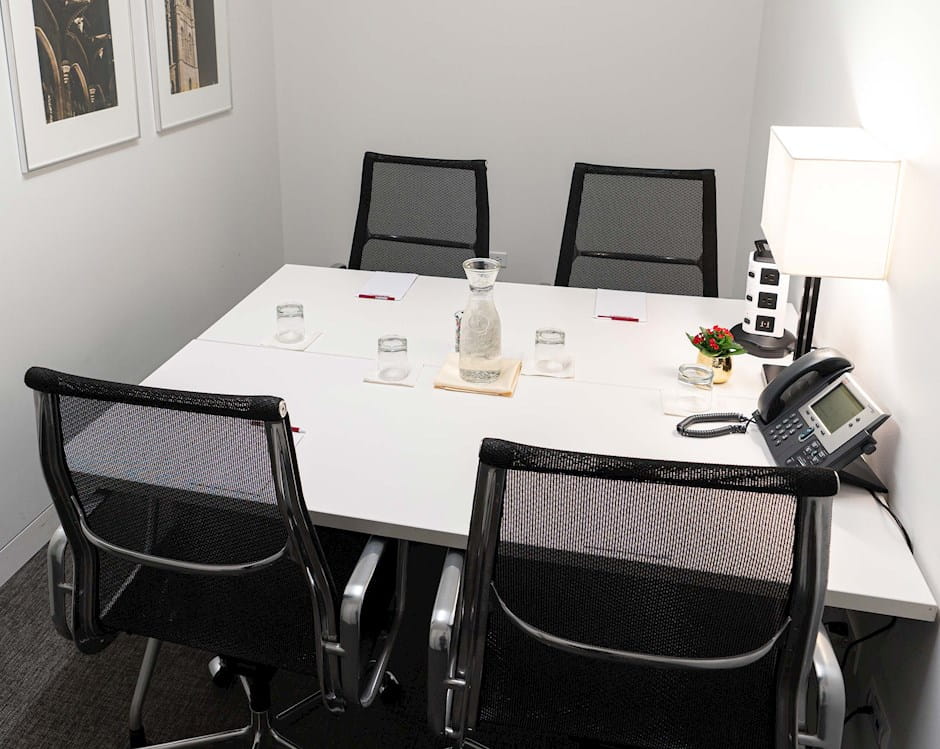 PIMCO small executive board room with 4-person table set with water, notepads, and outlets