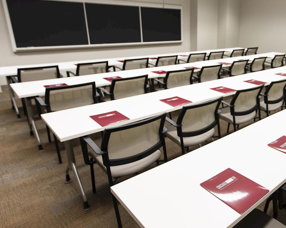 Classroom 203 at the University of Chicago Gleacher Center from the entrance with 3 rows of tables and chairs in front of a blackboard