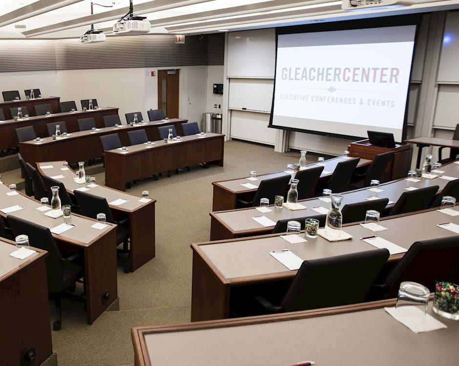 A view of the Gleacher Center room 406 from the back looking down on tiered tables and chairs in a semi-circle